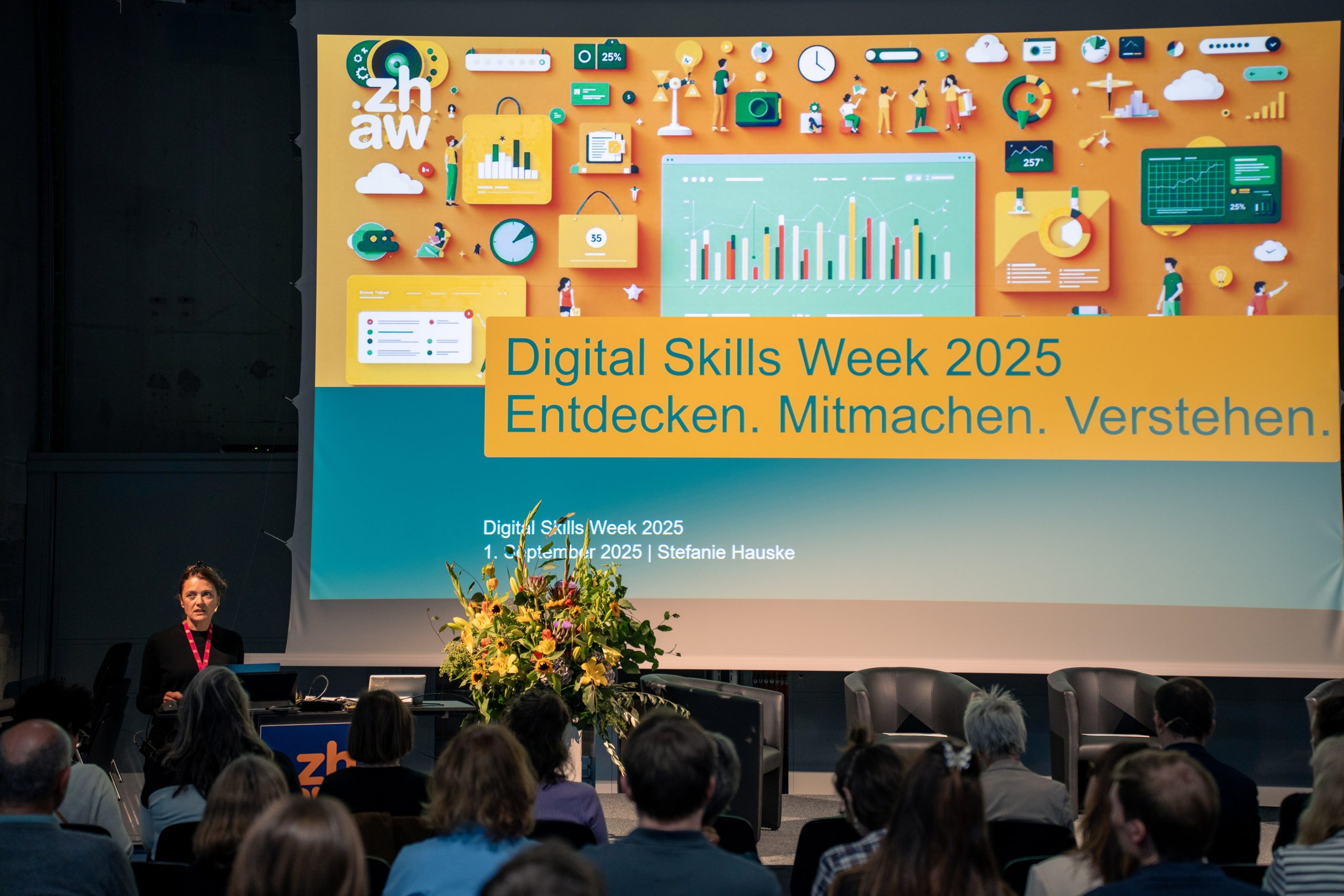 Foto der Bühne an der Digital Skills Week mit Stefanie Hauske am Rednerpult, im Vordergrund das Publikum.