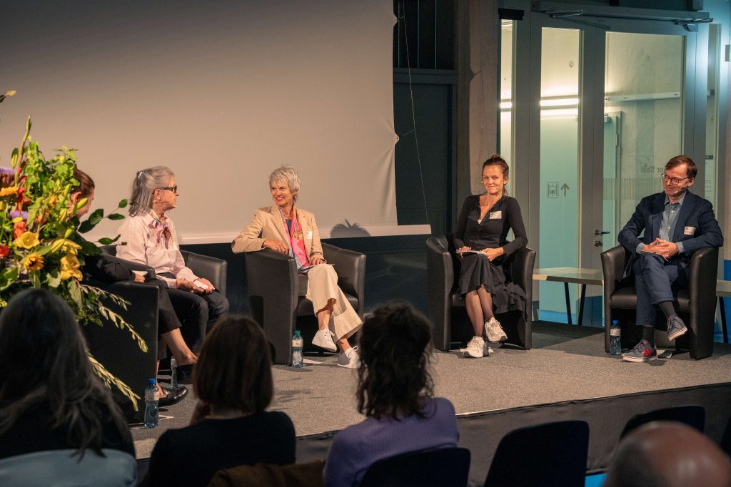 Foto der Personen am Panel auf der Bühne, die miteinander diskutieren.