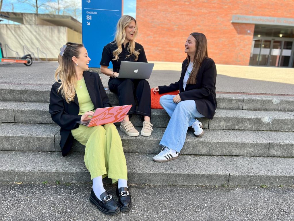 Drei Studentinnen sitzen draussen vor der ZHAW und besprechen Content-Ideen.