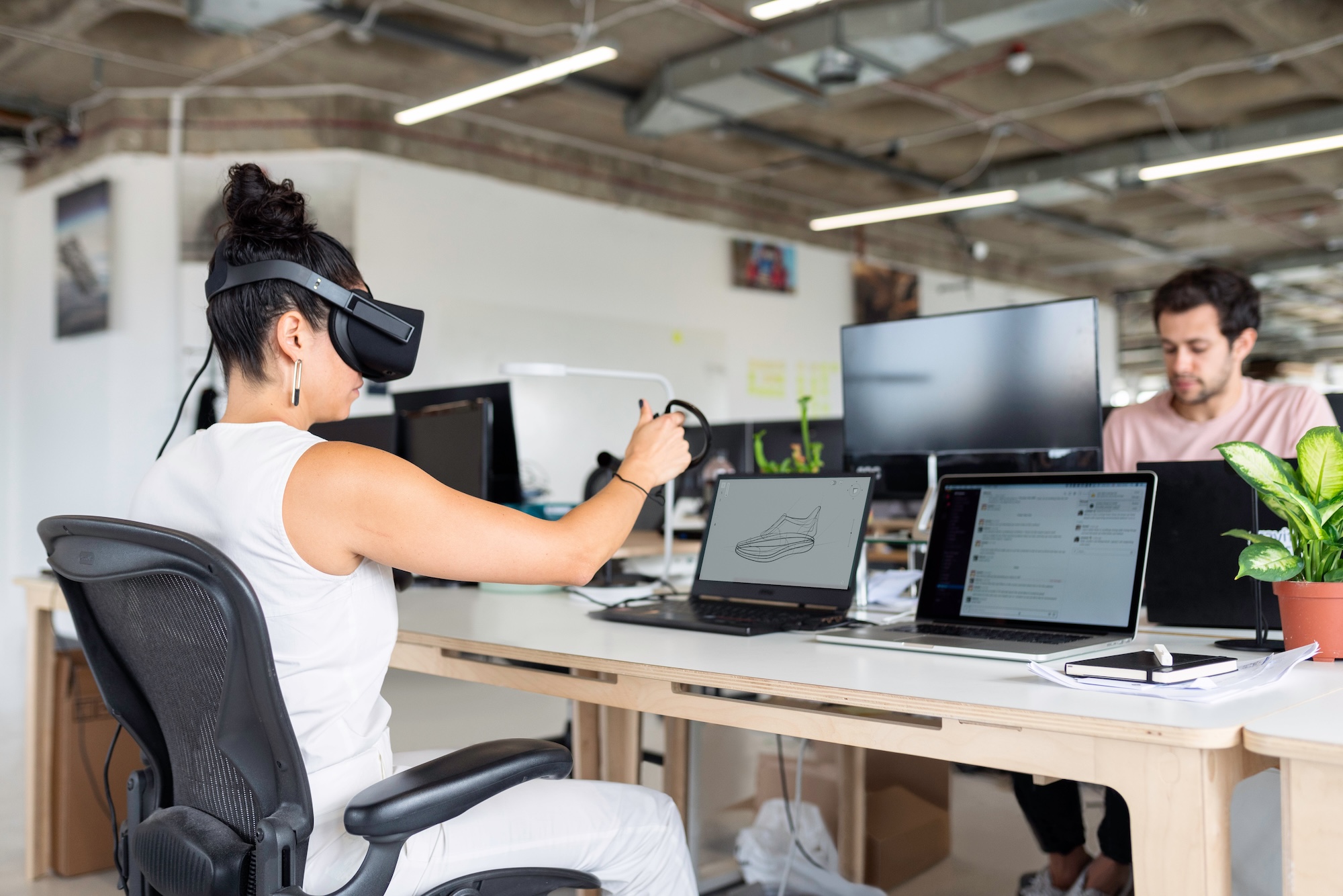Symbolbild mit einer Frau, die eine VR-Brille aufgesetzt hat und vor einem Bildschirm sitzt.