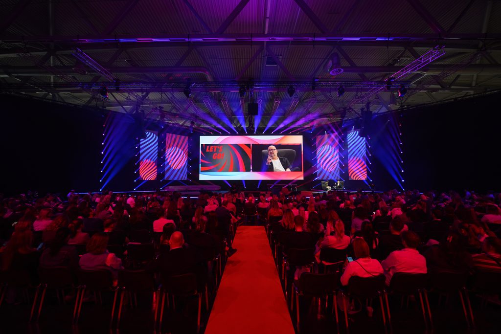 Voll besetzter Saal vor einer rot beleuchteten Bühne an der DMEXCO 2026.