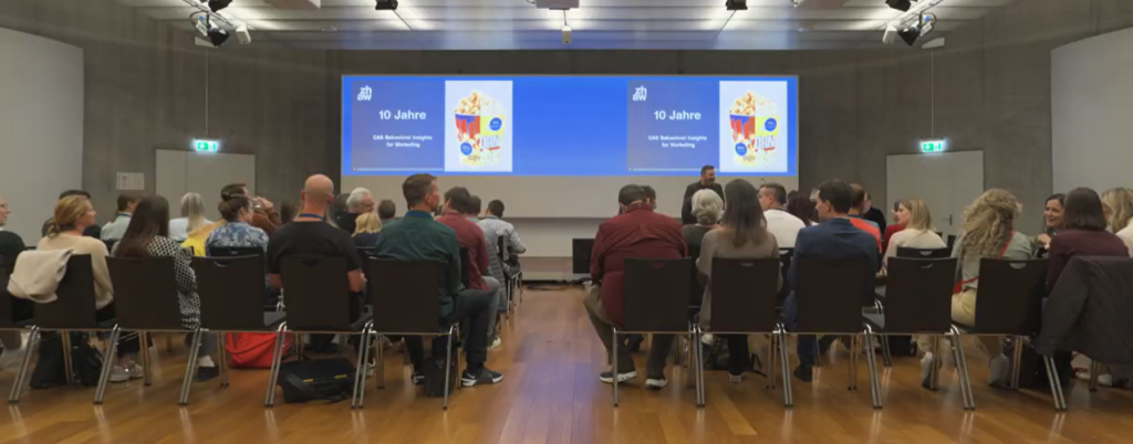 Gäste des Jubiläumsanlasses vor der Leinwand mit der Folie «10 Jahre CAS Behavioral Insights for Marketing».