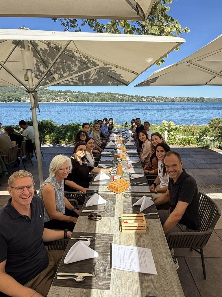 Teilnehmende und Dozierende des CAS sitzen beim Mittagessen auf einer Terrasse mit Blick auf den See