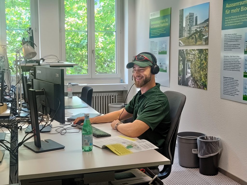 Noah Mulheim arbeitet als Projektleiter Stadtgrün/Naturberatung bei Grün Stadt Zürich an seinem Schreibtisch. Er sitzt am Pult und blickt auf seinen Computerbildschirm in einer Büroumgebung.