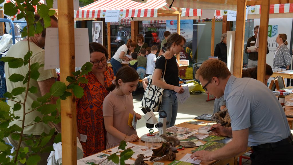 Besucher:innen am Klimamarkt in Vorarlberg informieren sich an verschiedenen Ständen über Klimaschutz und Biodiversität.