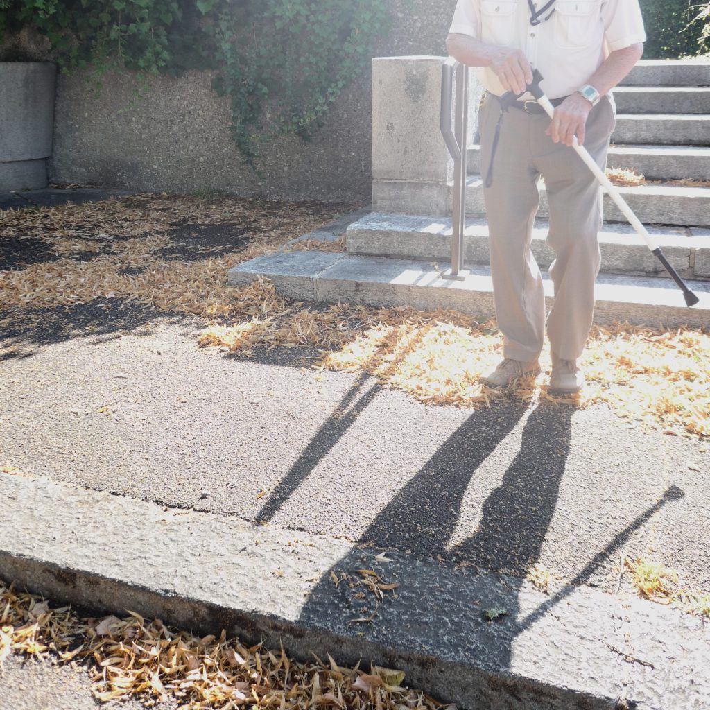 Ein Mann mit Gehstock geht von einer Treppe am Friedhof, die als physische Barriere den Zugang für Menschen mit Mobilitätseinschränkungen erschwert.
