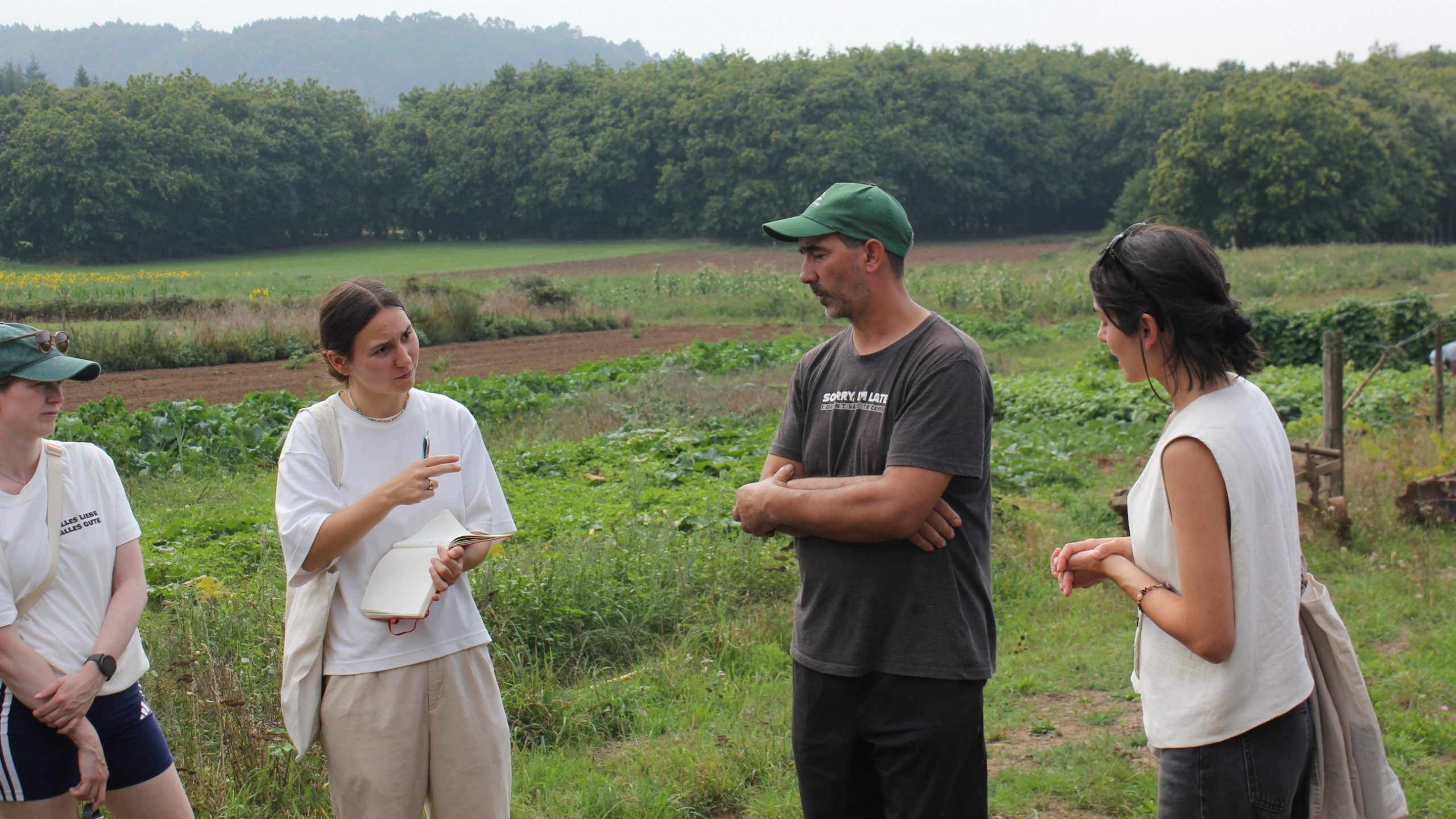Teilnehmende der Agrobiodiversity Summer School 2026 im Austausch mit einem Landwirt auf einem vielfältig bewirtschafteten Feld in Galicien.